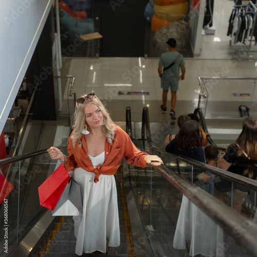 Portrait of a beautiful woman with shopping bags in the mall on the escalator and looking to the side. Young shopaholic.