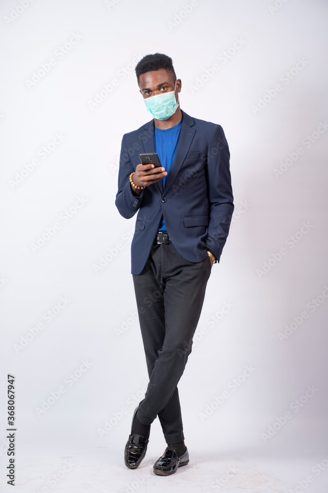 a young african business man wearing a suit and face mask using his mobile phone a young african business man wearing a suit and face mask using his mobile phone