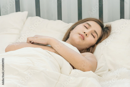 Beautiful Asian woman sleeping on the bed in the cozy white bedroom with morning light. Sleep, Relax, dream, Sick, Rest. © Naparat