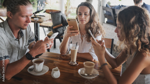Young group of friends in a cafe drinking coffee, everyone is looking at the smartphone screen, communication problems, modern technologies, a new normal lifestyle
