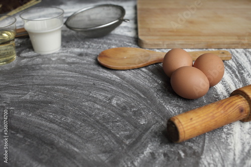 Egg, flour, olive oil, milk, wheat ears, kitchen tool on gray table background.