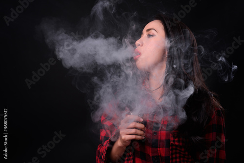 Young beautiful Asian woman vaping against black background © Ranta Images