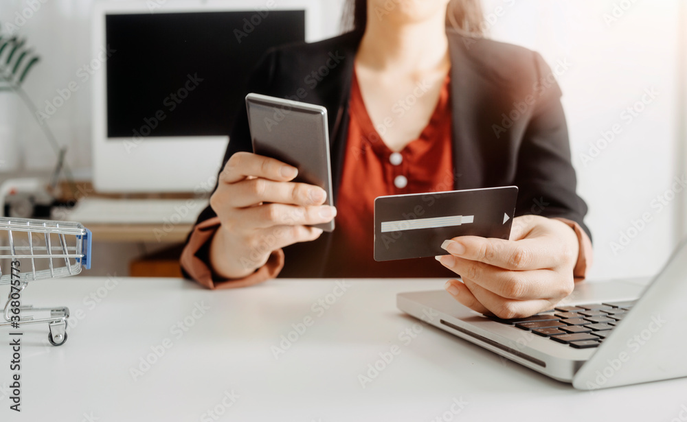 Fototapeta premium businesswoman hand using smart phone, tablet payments and holding credit card online shopping, omni channel, digital tablet docking keyboard computer at office in sun light