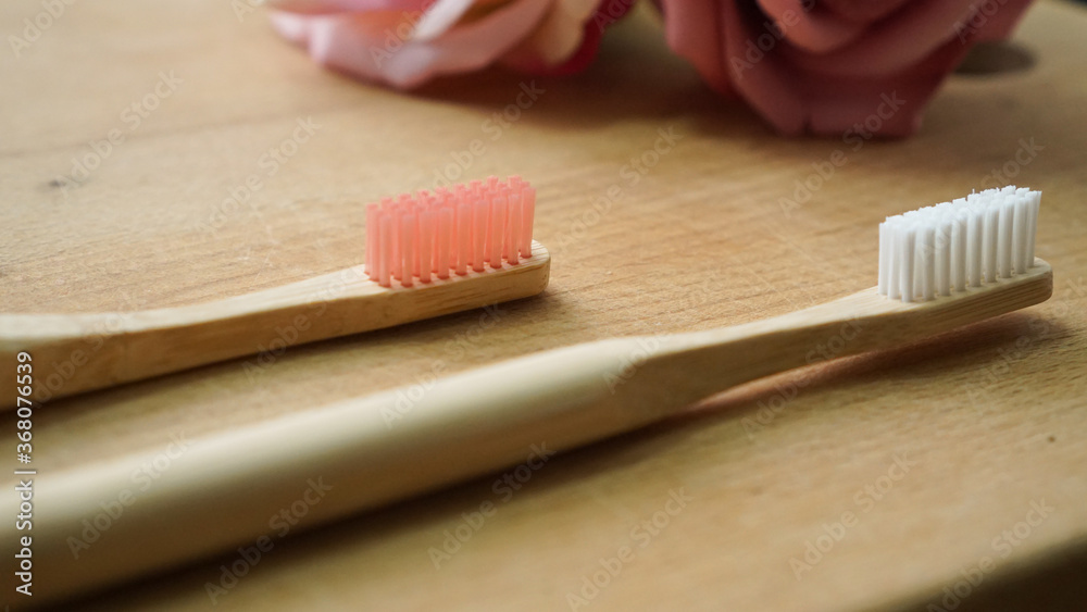 Eco-friendly bamboo toothbrush with blurred pink bamboo toothbrush and roses on a wood background. Natural organic dental concept Eco-friendly bamboo toothbrush with blurred pink bamboo toothbrush and roses on a wood background. Natural organic dental concept