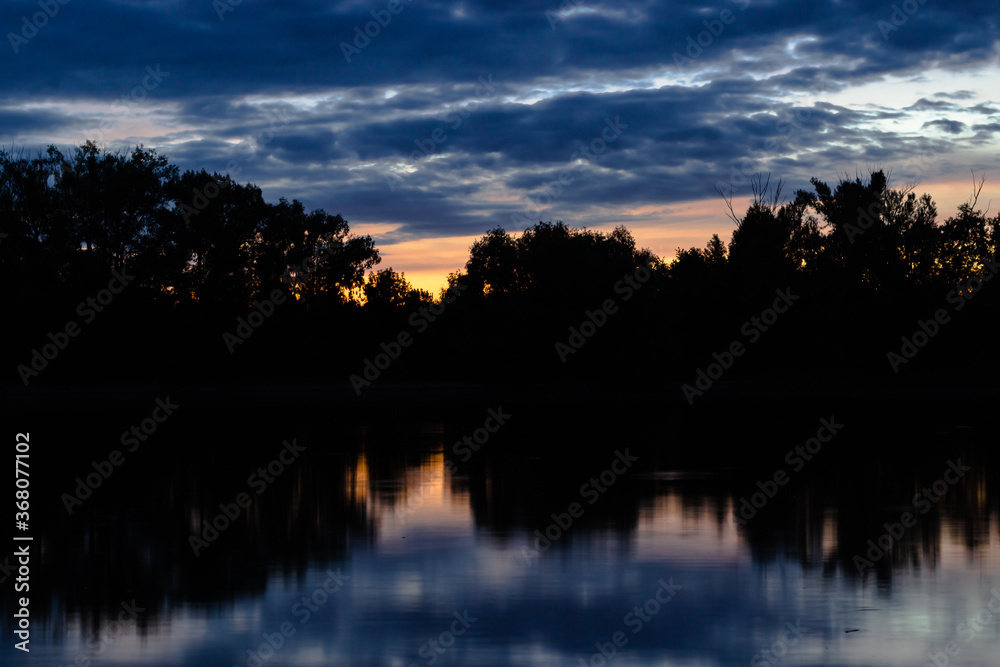 Fototapeta premium Sunset on the Volga river. View of one of the islands (the contours of trees against the sky) on the Volga from the shore during sunset.