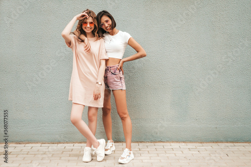 Two young beautiful smiling hipster girls in trendy summer clothes.Sexy carefree women posing on street background in sunglasses. Positive models having fun and hugging