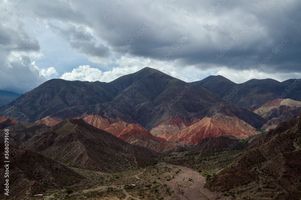 Andes Mountain range. Aerial view of the colorful mountains, desert and valley under a cloudy sky in Tilcara, Argentina. 