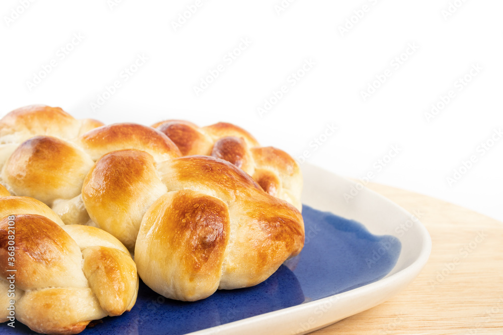Multiple small braided buns. White yeast bread with egg wash on blue and white plate. Perspective view. Authentic Swiss butter bread recipe called Zopf or Butterzopf. Isolated on white.