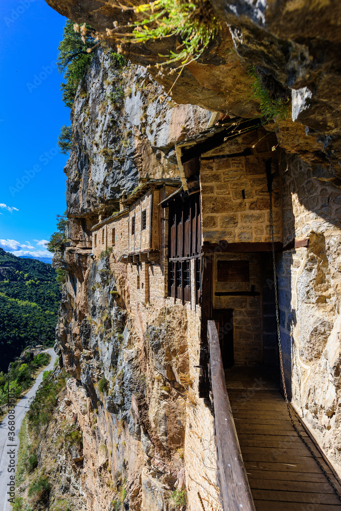 View of Holy Kipinas Monastery. The entrance to the monastery is via a suspension bridge.The monastery was built in a cliff overhanging a narrow mountain road and a deep gorge. Tzoumerka, Greece View of Holy Kipinas Monastery. The entrance to the monastery is via a suspension bridge.The monastery was built in a cliff overhanging a narrow mountain road and a deep gorge. Tzoumerka, Greece