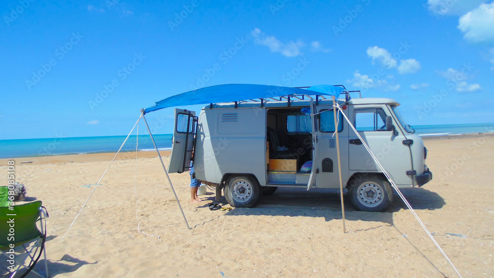 Fototapeta premium Camper on the beach with an awning from the sun. Vacation, clear, Sunny day. Camping.