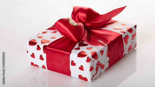 Gift box wrapped in white paper with red heart texture. And wrapped in a pink ribbon.