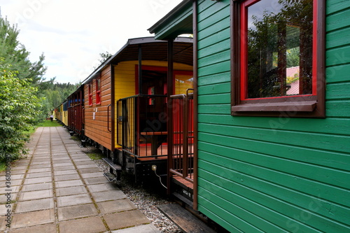 Close up on a set of colorful and vivid passenger comparments made out of metal and wood standing on a side track next to a dense forest or moor seen on a Polish countryside in summer