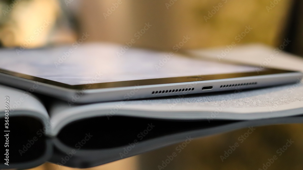 An open magazine and tablet on a glass black coffee table. Blurred bokeh background, close-up. Light interior with sunlight, sunset, bokeh. An open magazine and tablet on a glass black coffee table. Blurred bokeh background, close-up. Light interior with sunlight, sunset, bokeh.