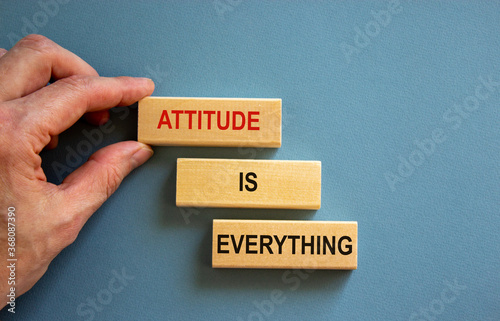 Wooden blocks form the words 'attitude is everything' on blue background. Male hand.