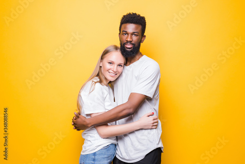 Portrait of romantic multiracial couple embracing, posing together and smiling at camera over yellow background