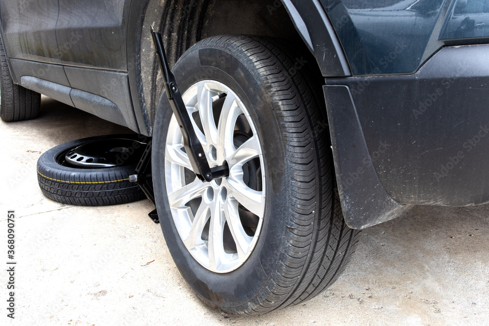 an original equipment manufacturer supplied OEM tire wrench on a lug nut on a cast aluminum wheel on a car on a jack