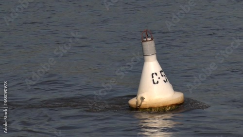 A white buoy on the river sways under the pressure of the current of water