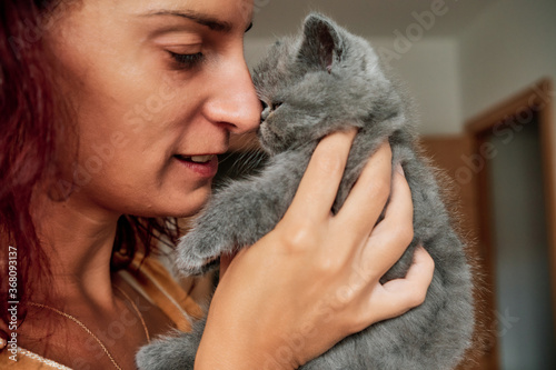 young woman playing with cute little grey cat - pet care concept