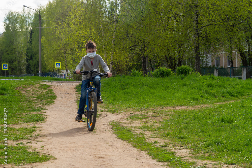 one teenager alone in the middle of the street rides a blue Bicycle. A fastidious person puts on a surgical mask to prevent any type of virus or disease, such as coronavirus or covid - 19.