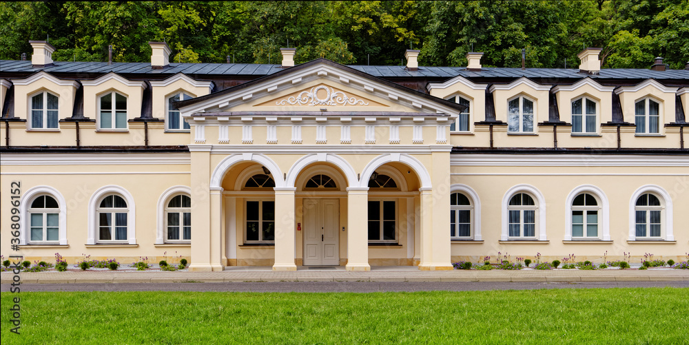 Facade of neoclassical architecture style building in European town. Sunny day in park in Naleczow health resort in Poland.