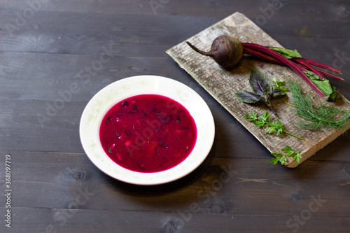 Cold red beetroot soup in white plate on black wooden background with ingredients on board