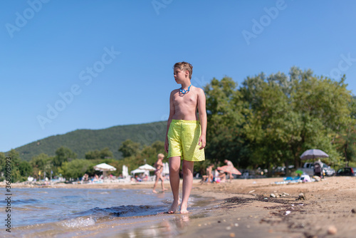 Young blond teenage boy is walking on a beach