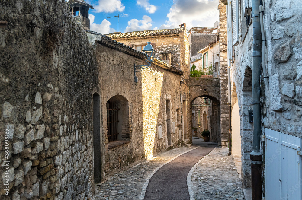 An empty narrow cobblestone street sloping down to a covered archway in the mountaintop medieval village of Saint Paul de Vence, in Southern France