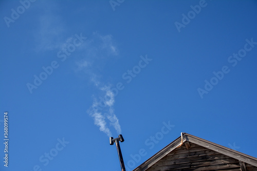 木造の山小屋の、金属製のH形の煙突から立ち昇る、薪ストーブの煙。青空。旅行、行楽、旅、シルバーウィーク、秋晴れ。冬晴れ。 photo