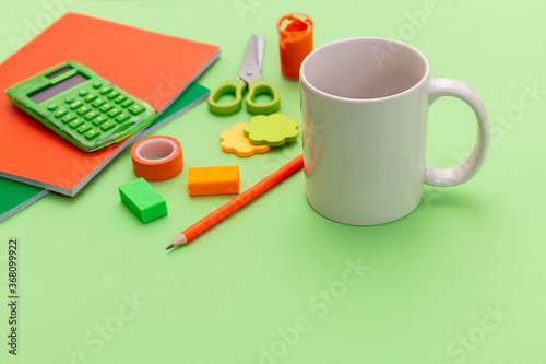 Mug white color and school supplies on green background. Kids homework soft drink