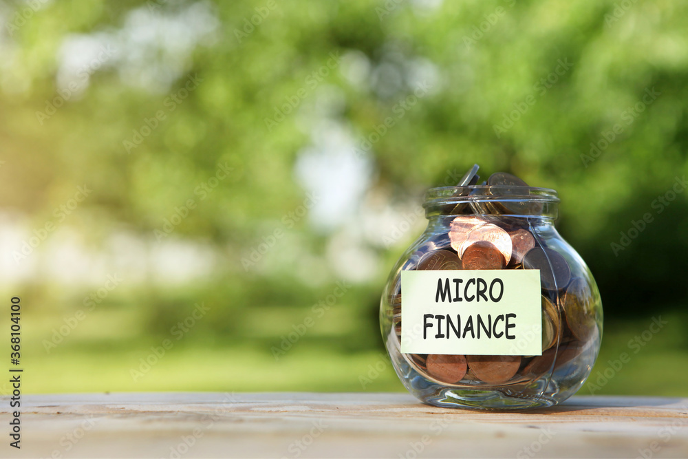 Micro finance. Glass jar with coins, on a wooden table, on a natural background.Investment and finance concept.