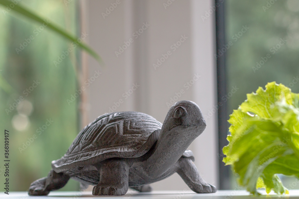 a lazy small brown iron turtle on a white surface in front of a green salad leaf by the window, idea of slow living, slow eating, enjoying countryside lifestyle, keeping artificial animal at home a lazy small brown iron turtle on a white surface in front of a green salad leaf by the window, idea of slow living, slow eating, enjoying countryside lifestyle, keeping artificial animal at home