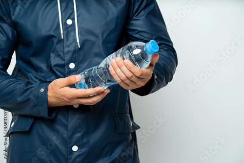 a plastic bottle filled with clean water with a lid, in the hands of a man in a raincoat from the rain. well-groomed male hands