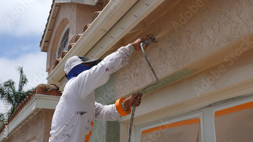 Foto Professional contractor using a spray paint gun to paint the stucco on a home