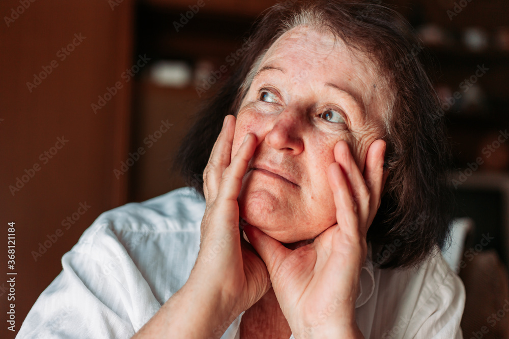 Close-up portrait of an elderly woman, hands on her head, looking worried Close-up portrait of an elderly woman, hands on her head, looking worried