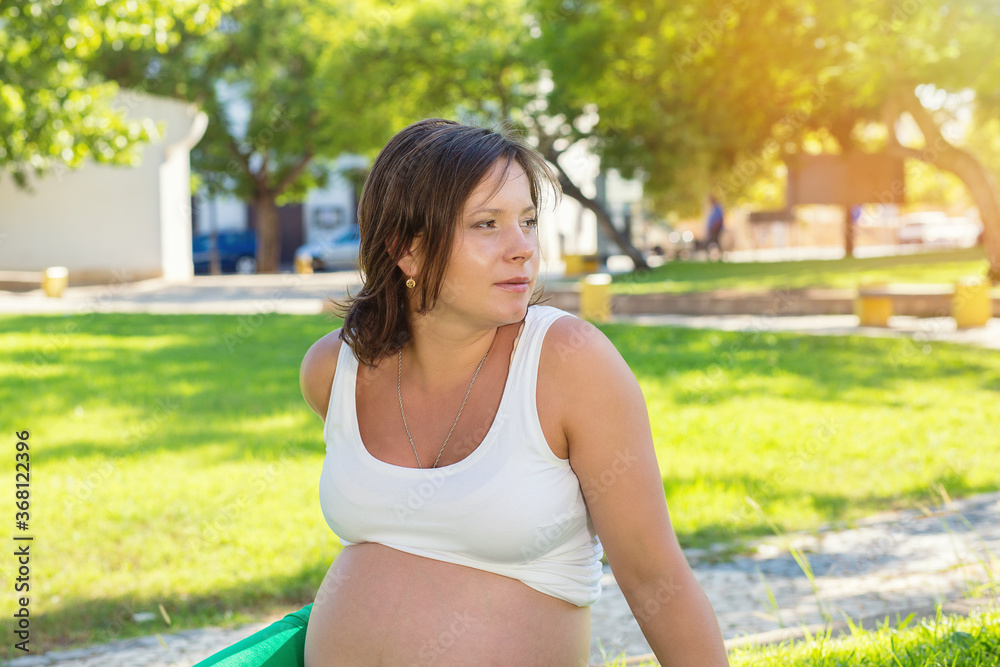 pregnant woman looking to the side sitting on a green grass lawn pregnant woman looking to the side sitting on a green grass lawn