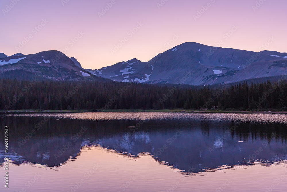 Sunset with pink sky behind mountains, lake and evergreen trees