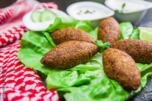 Delicious Lebanese  food, kibbeh (kibe) with sauces and lemon on black slate stone and granite background with traditional keffyeh. photo