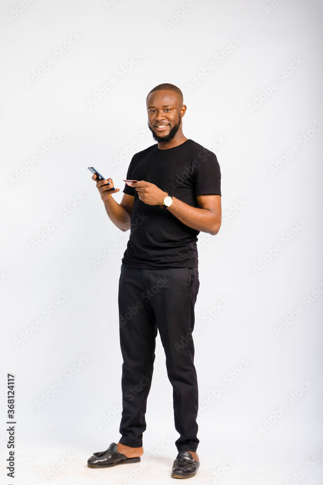 young black handsome man standing using his credit card to pay for something on his smartphone young black handsome man standing using his credit card to pay for something on his smartphone
