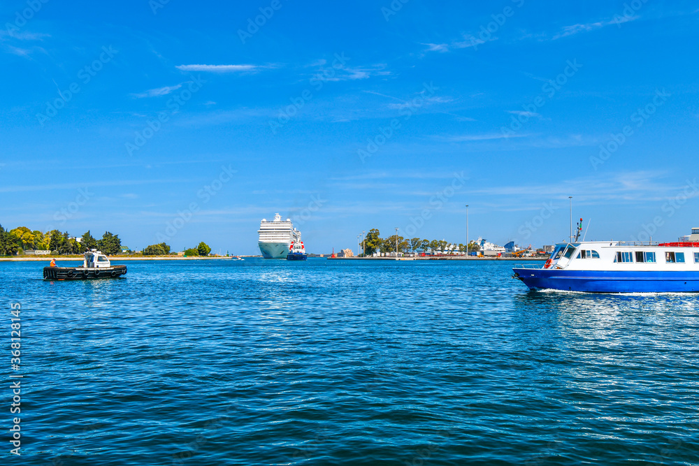 A large cruise ship pulls into the Brindisi Italy harbor and cruise port on a summer day in the Puglia area of the Mediterranean.