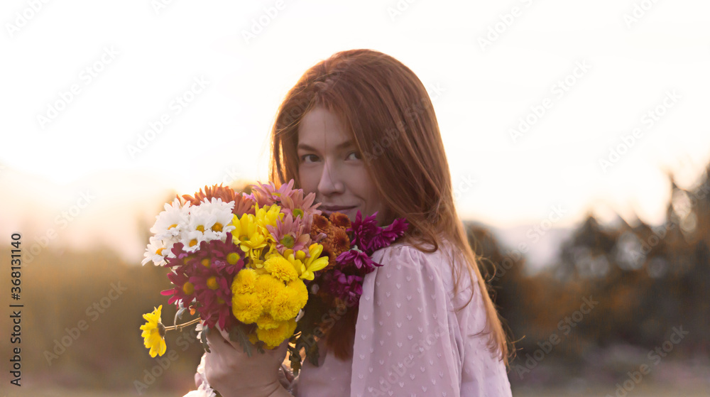 Red haired girl holding different colors of flowers in the sunset Red haired girl holding different colors of flowers in the sunset
