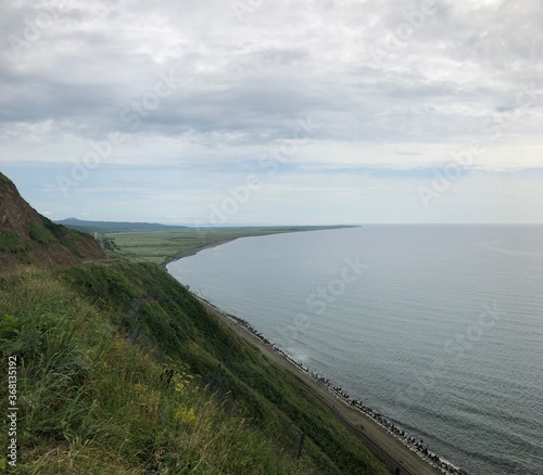 Wallpaper Mural A scenic coastal view from a grassy cliff on Sakhalin Island, overlooking the calm sea that stretches to the horizon under a cloudy sky. Torontodigital.ca