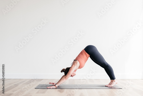 Woman in downward dog yoga pose in white yoga studio