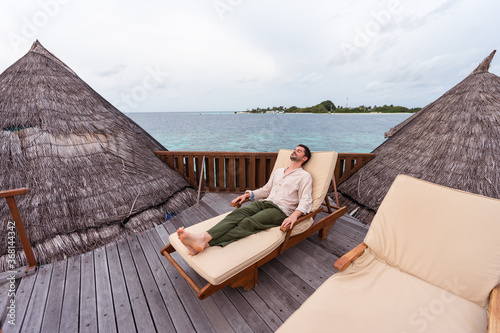 Obraz na płótnie western young man lying on deckchair over water hut at luxury resort in maldives with sea in the background w salonie