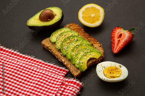 delicious and healthy breakfast of avocado sandwich with egg, strawberry and lemon on black background