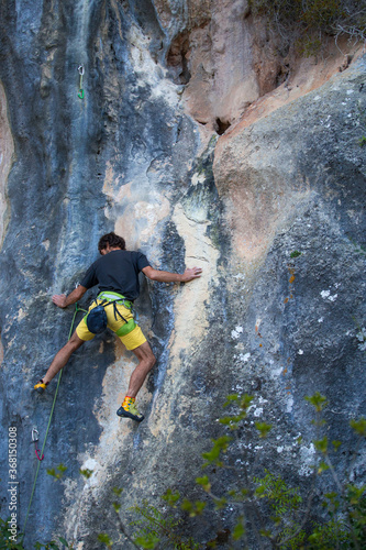 A strong man overcomes a difficult climbing route on a natural terrain.