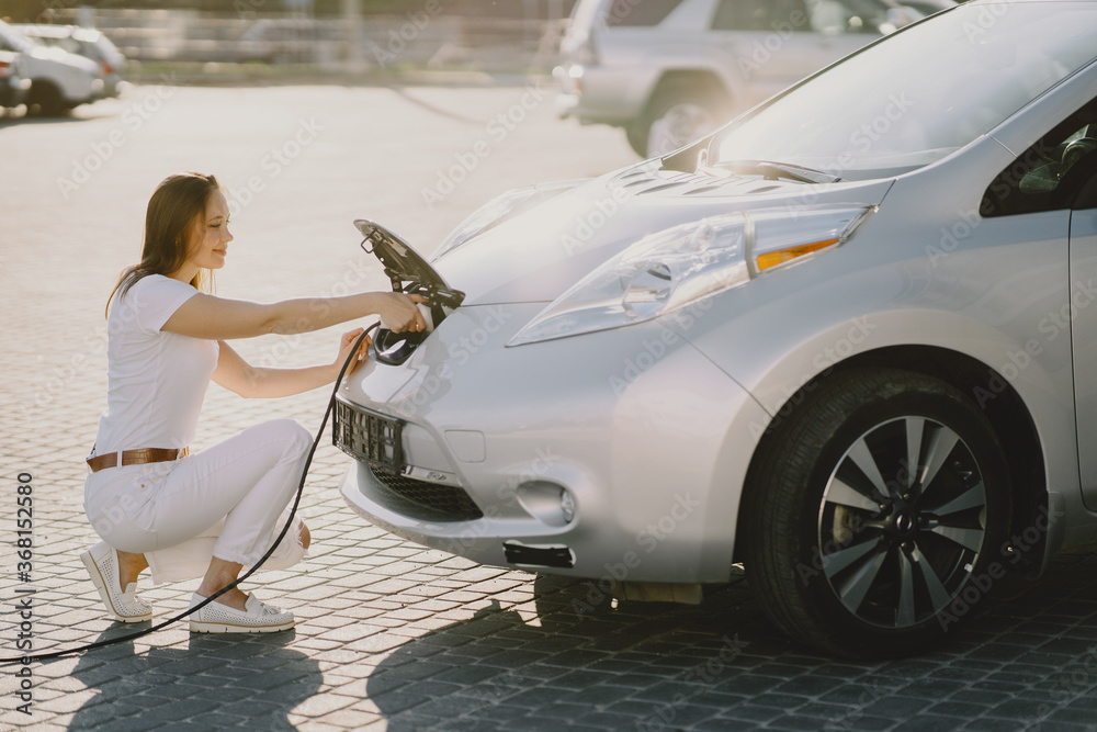 Fototapeta premium Charging electro car at the electric gas station. Woman standing by the car.
