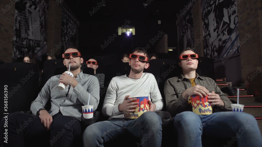 Three friends with 3D glasses are watching a movie and eating popcorn