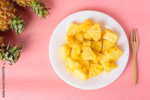 Sliced pineapple fruit on white plate with fork ready to eating on pastel pink background, Tropical fruit