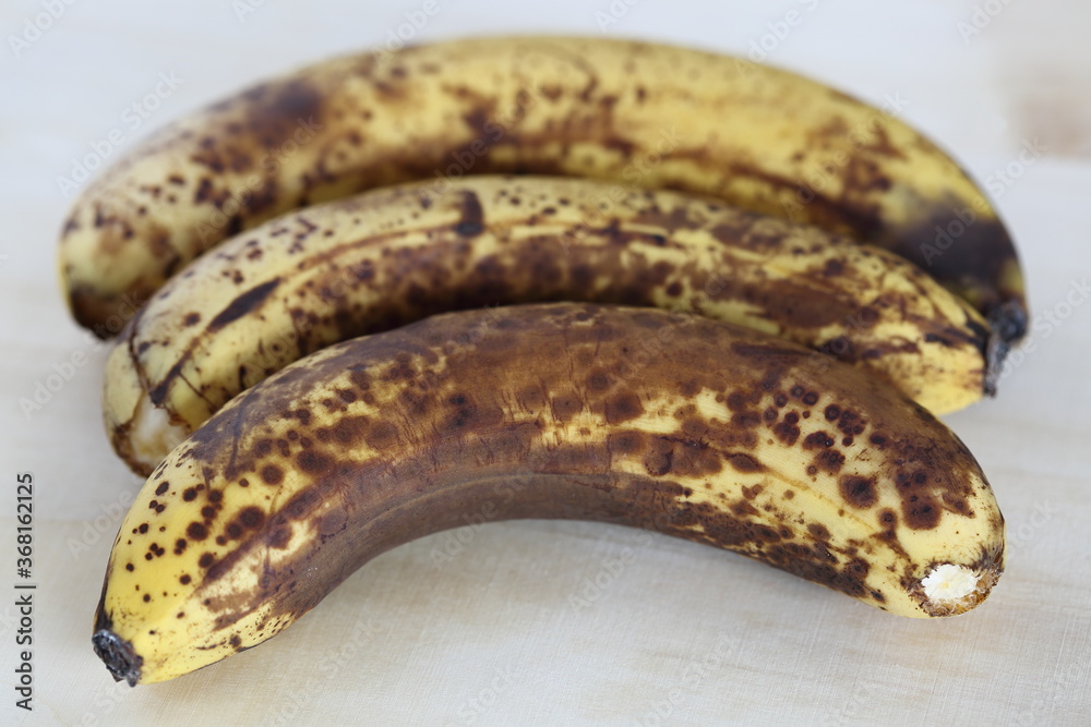 Rotten bananas with dark spots on theirs skin close up lie on table