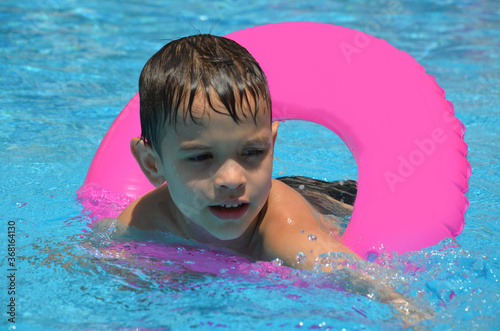 Happy baby boy in a swimming pool with inflatable circle. Cute little baby having fun in the pool. On open air. Sport activities for children. photo